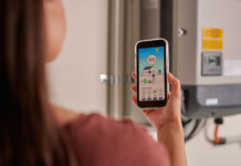 Survey shows 76% of households trying to lower energy use Woman with long dark hair holds smart phone with energy usage app while standing in front of solar inverter