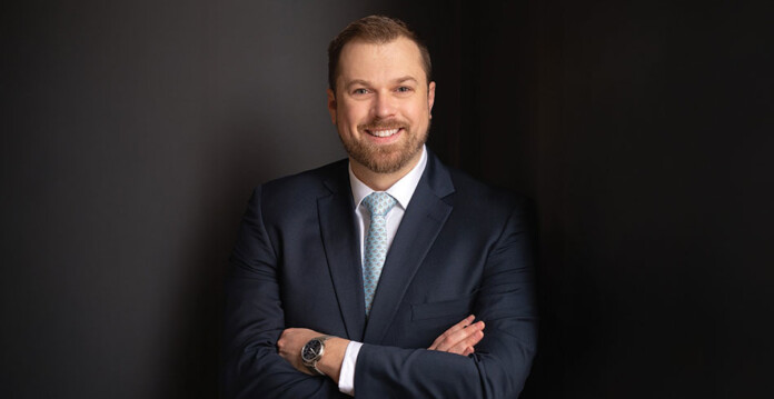 Man wearing business suit and tie stands for photo in front of dark grey backdrop