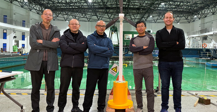 Five researchers stand with a floating wind turbine prototype at a wave testing facility in China