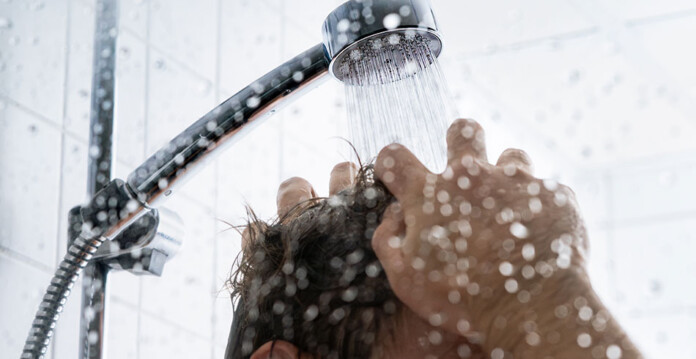 Shower head spraying hot water on the top of a male head