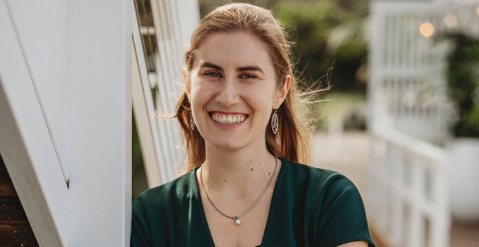 Head and shoulders shot of smiling woman wearing dark green dress outside in sunshine
