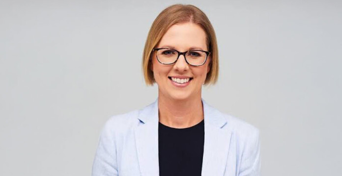 Head and shoulders shot of smiling female executive wearing a pale blue suit jacket and dark eyeglasses