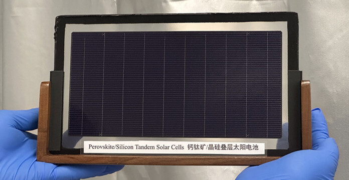 Blue-gloved hands hold up tandem solar cell prototype