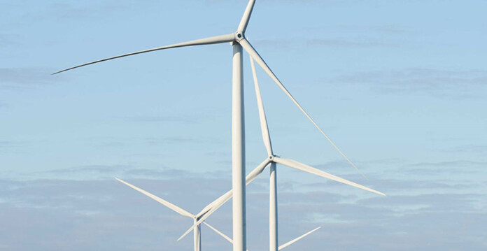 Three large white wind turbines pictured against pale blue sky