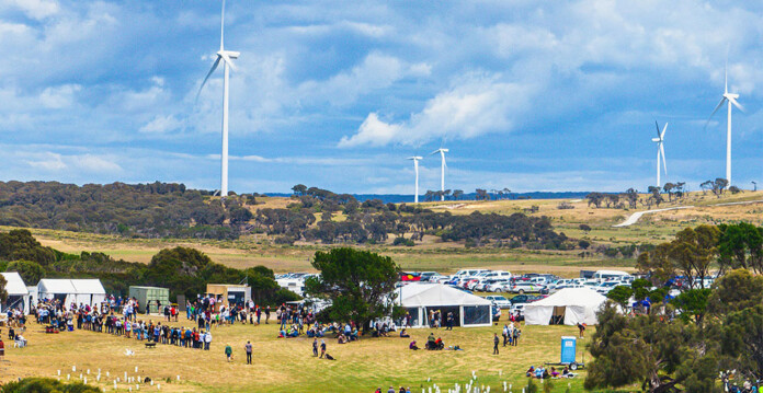 Aboriginal festival with tents and people and wind turbines in the background