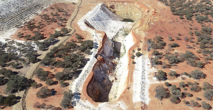 Aerial shot of a large open-cut gold mine surrounded by red dirt and scrub