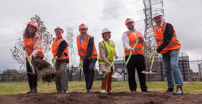 Energy executives in safety gear and hard hats hold shovels as they turn ground at the site of a battery storage system