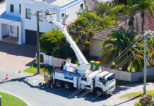 Consumer groups say energy networks profiting from RORI Utility worker in a crane bucket works on power line in residential street