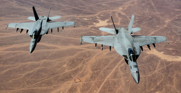 Two U.S. Navy FA-18 Super Hornets flying over arid landscape