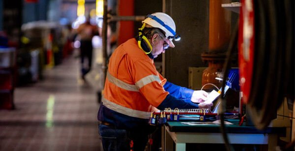 Male worker in safety wear and hard hat works on laptop inside power station