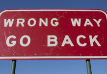 Hey Minister, wrong way—go back! Large red road sign saying WRONG WAY GO BACK with blue sky overhead