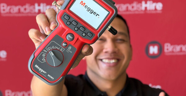 Smiling man holds up a Megger testing unit 