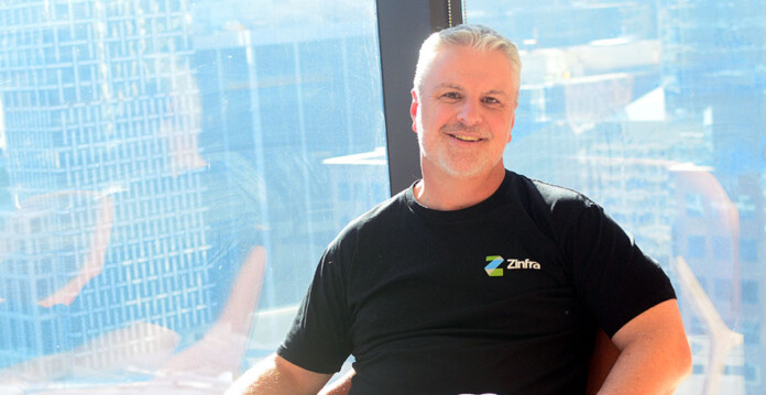 James-Quigley-Zinfra Zinfra's James Quigley wears black Zinfra shirt while sitting in a chair in front of an office window overlooking a city view