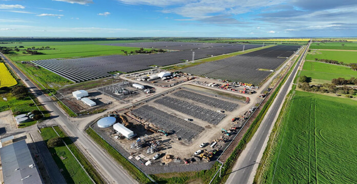 Aerial shot of solar farm surrounded by green grass with blue sky overhead