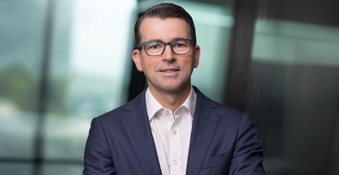 Head and shoulders shot of smiling male executive Stephen Harty wearing glasses and a dark business suit
