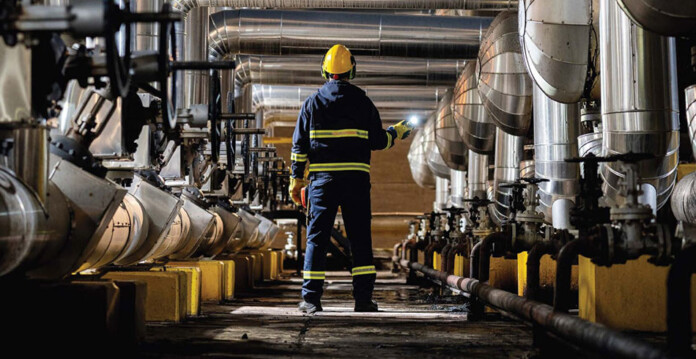 Worker in safety gear stands in centre of room with industrial heat plant