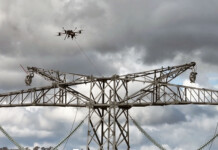 Drones and choppers form high-tech team at HumeLink A drone strings high-voltage cable onto a transmission tower with grey cloudy sky overhead