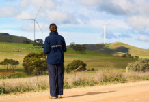 Neoen begins construction at Goyder North Wind Farm A woman in a Neoen-branded windcheater stands gazing out at a rural landscape with wind turbines on the horizon